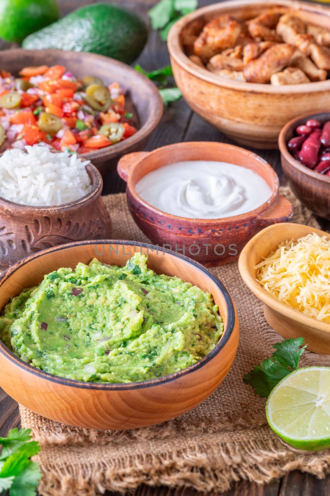 Bowls with burrito components: salsa, cheese, chicken, sour cream, lime, cilantro, rice, guacamole, beans, avocado, and chips