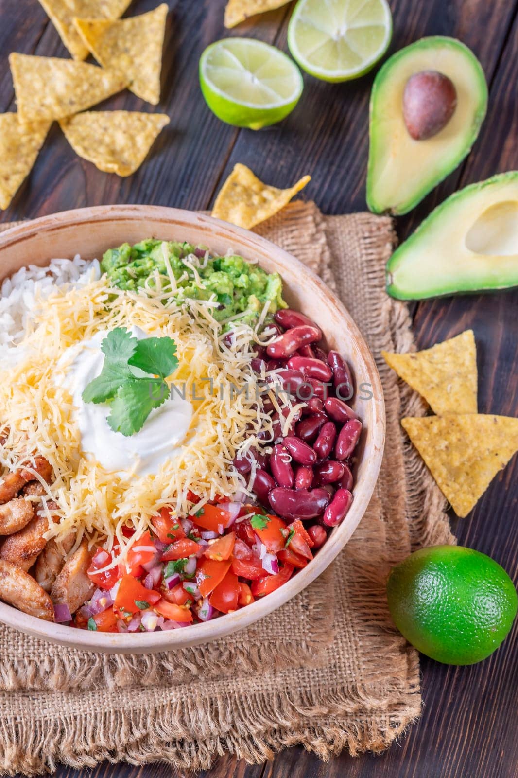 A large burrito bowl filled with chicken, rice, beans, guacamole, salsa, cheese, sour cream, and tortilla chips