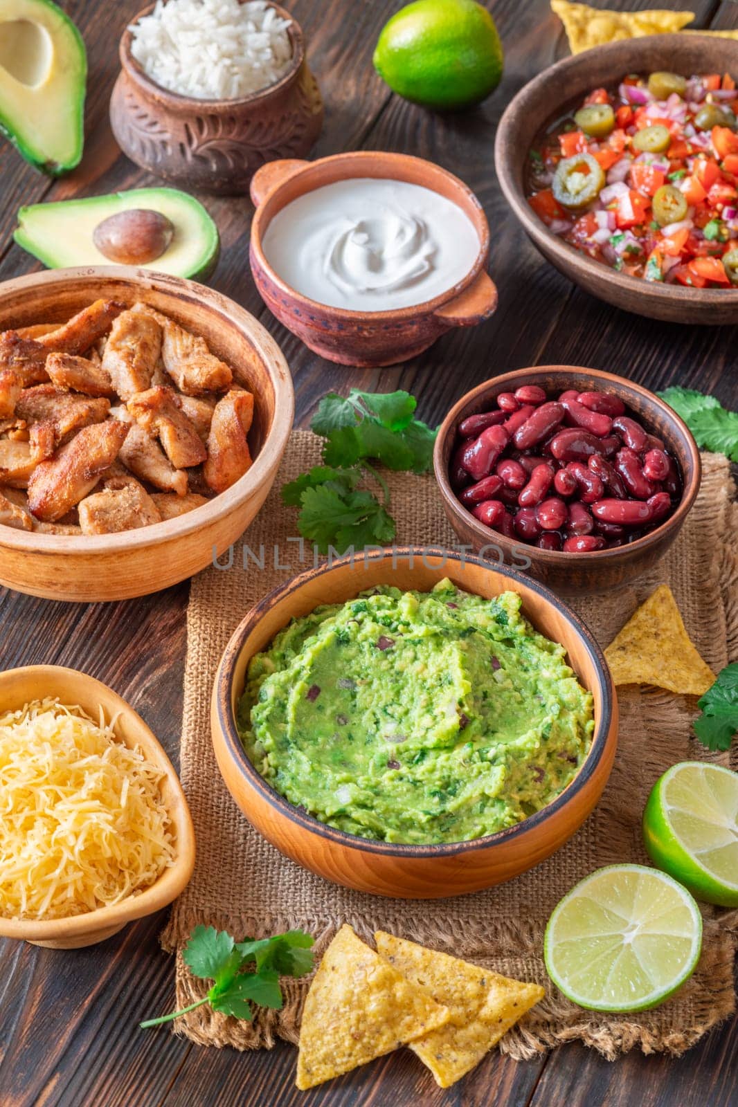 Bowls with burrito components: salsa, cheese, chicken, sour cream, lime, cilantro, rice, guacamole, beans, avocado, and chips