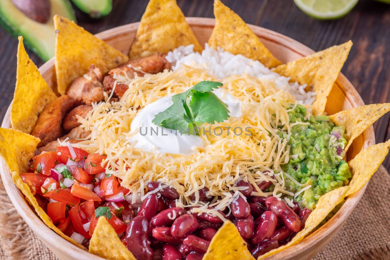 A large burrito bowl filled with chicken, rice, beans, guacamole, salsa, cheese, sour cream, and tortilla chips