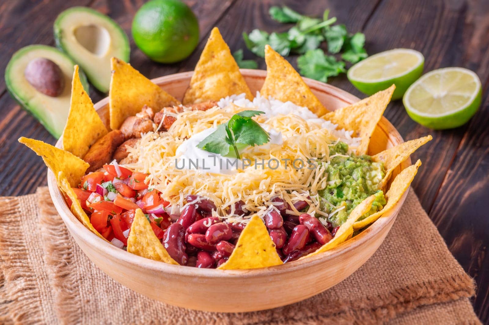 A large burrito bowl filled with chicken, rice, beans, guacamole, salsa, cheese, sour cream, and tortilla chips