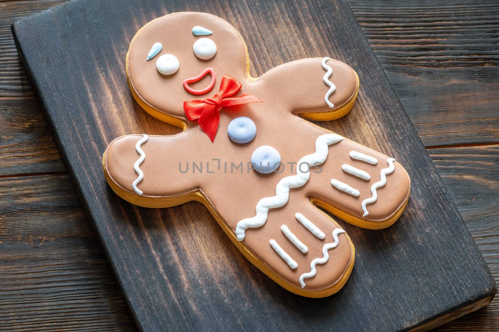 A large gingerbread man cookie with a red bow on a wooden cutting board