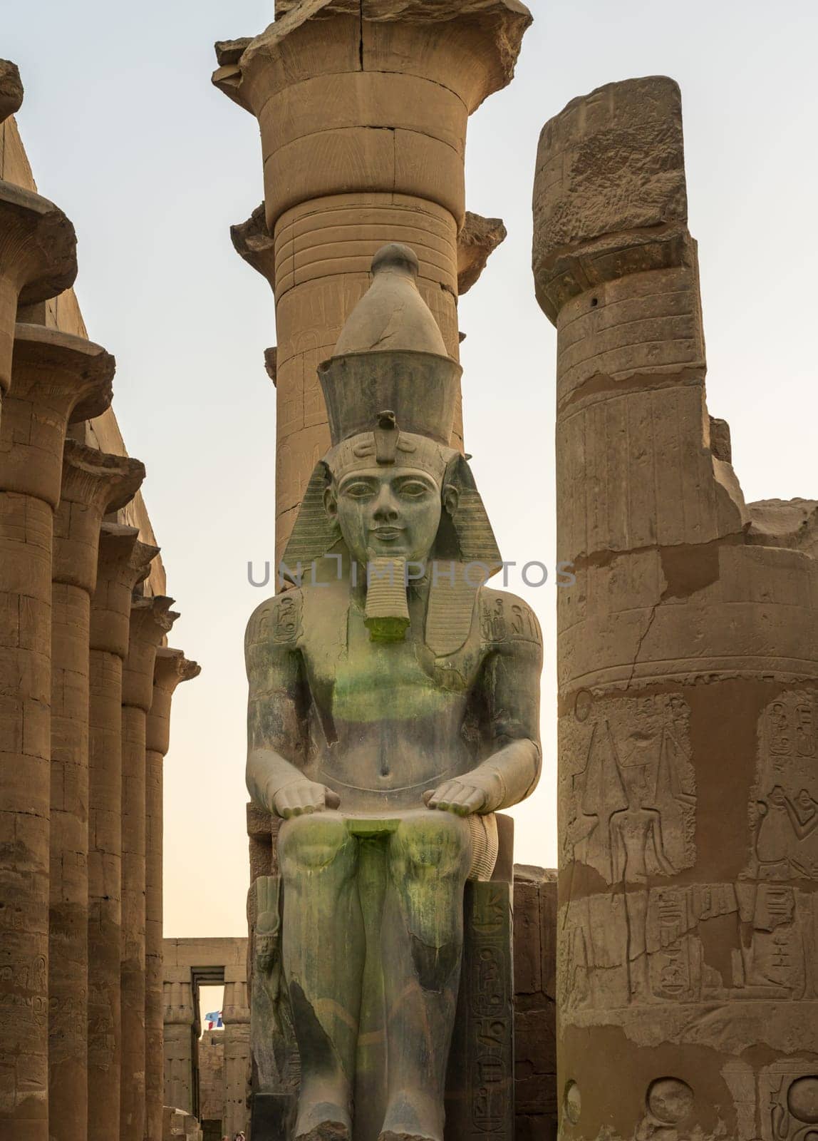 A massive stone statue of Ramesses II stands in Luxor temple, showcasing intricate carvings under the warm glow of the setting sun.