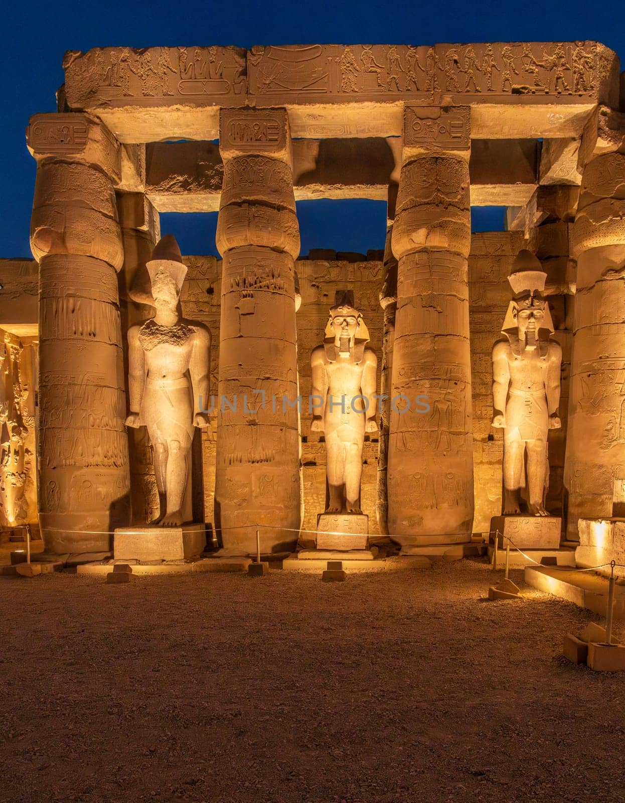 Massive numerous stone columns supporting roof with statues in Luxor Temple in Egypt illuminated at night