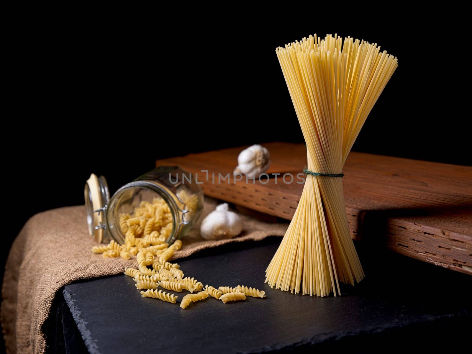 A still life photo of dried spaghetti and spiral noodles with two bulbs of garlic.
