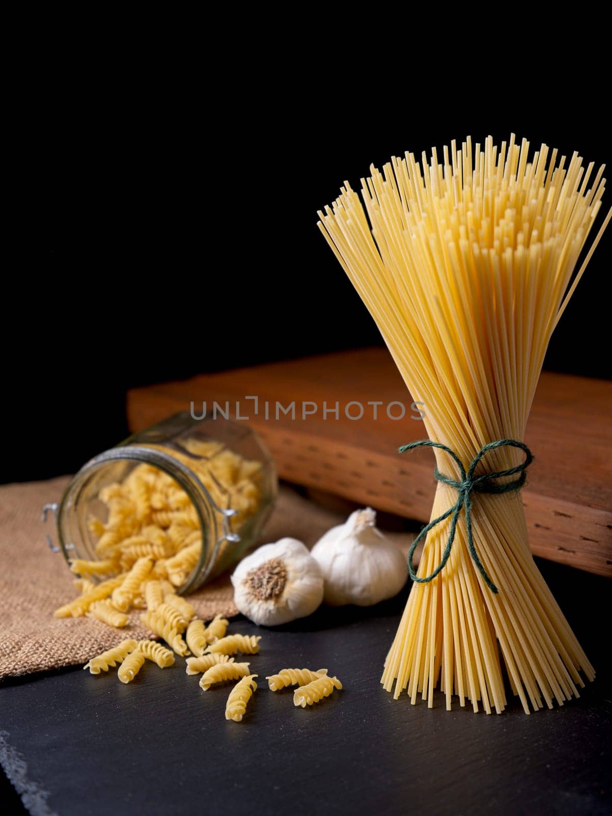 A still life photo of dried spaghetti and spiral noodles with two bulbs of garlic.