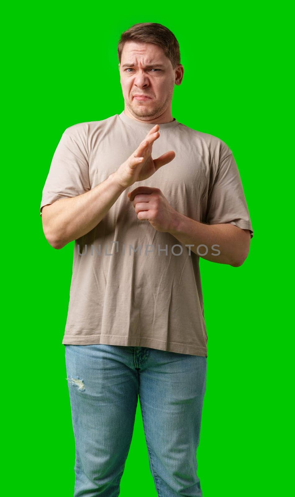 Young man making a disgusted expression while standing against a bright green background in studio