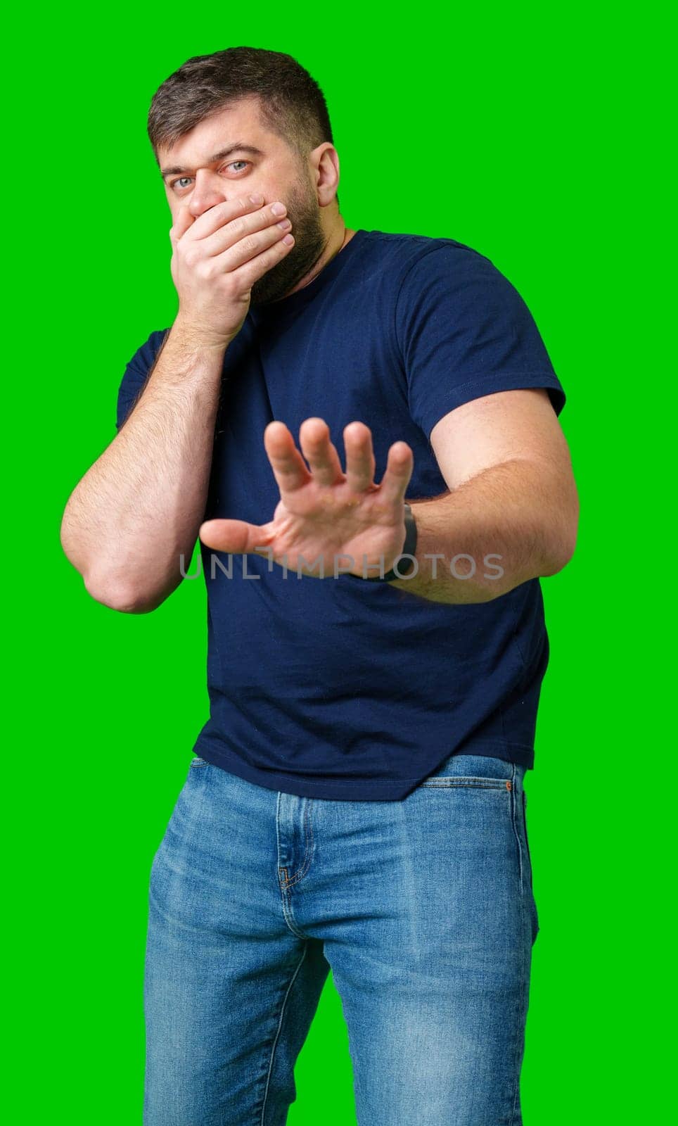 A man with a serious expression holds up both hands in a stopping gesture against a bright green background in studio