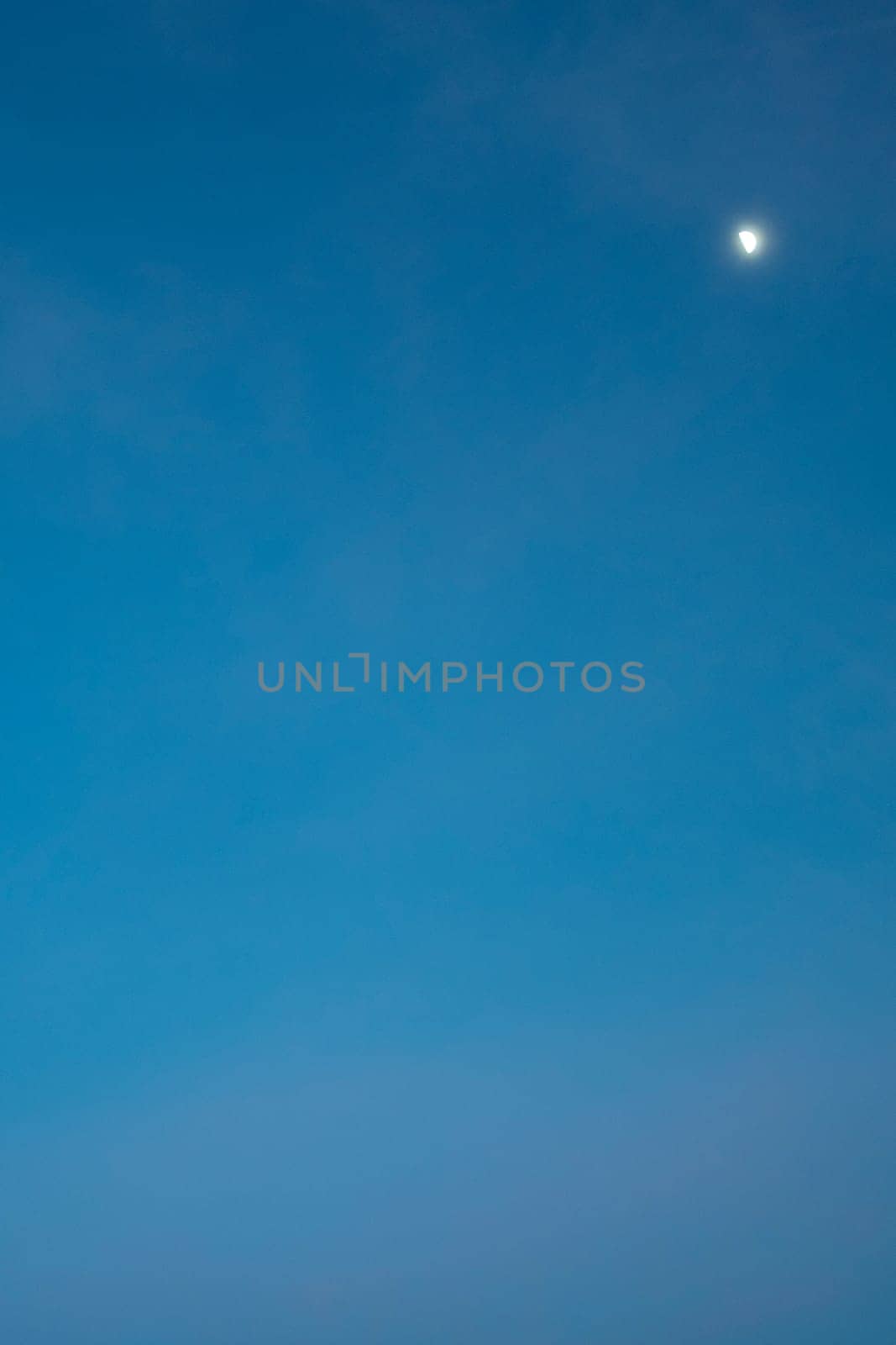 Clear blue sky with a visible crescent moon, creating a serene and unique daytime scene