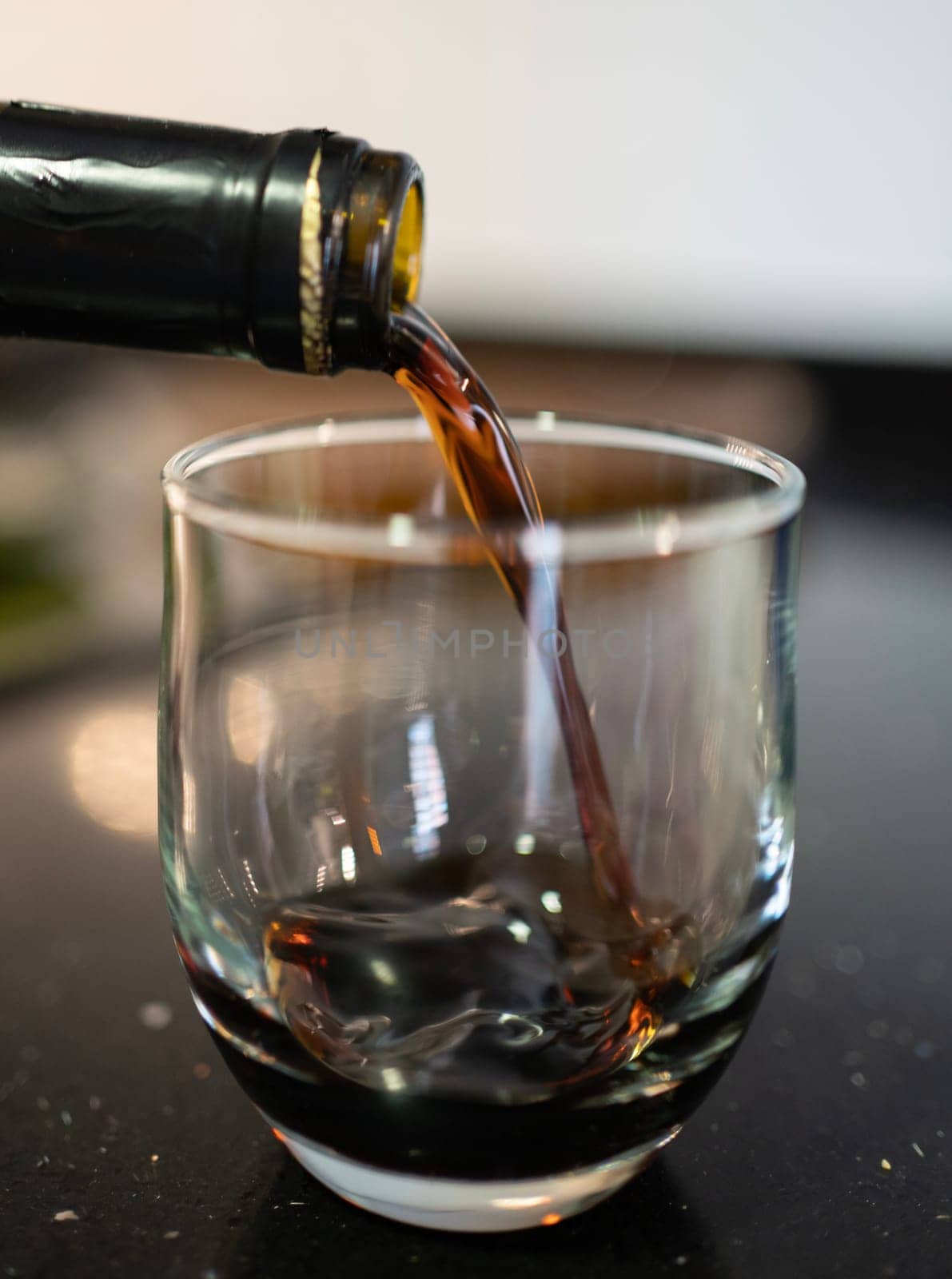 Red wine pouring from a bottle into a glass, creating a splash on a dark, reflective surface