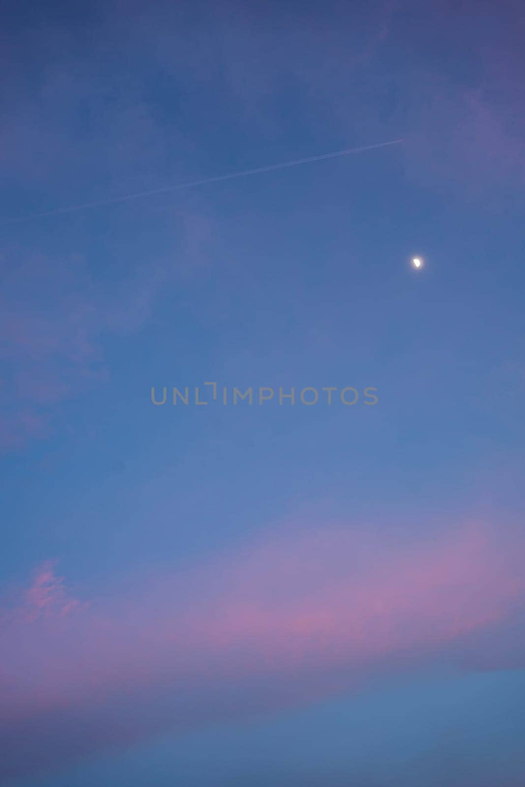 Airplane leaving contrail in colorful sunset sky with moon