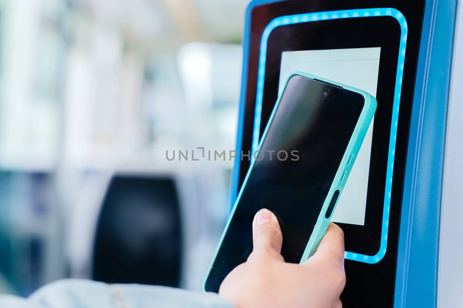 Close-up of a hand using a smartphone to scan a contactless ticket validator on public transport. The digital payment system enables quick and convenient access for commuters in a modern urban setting