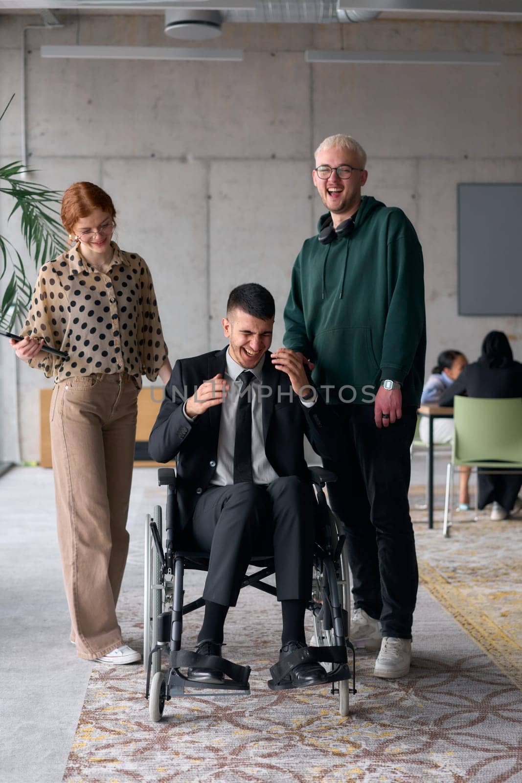 Group cheerful business colleagues, including a businessman in a wheelchair, posing together in a modern office, showcasing teamwork and inclusivity.