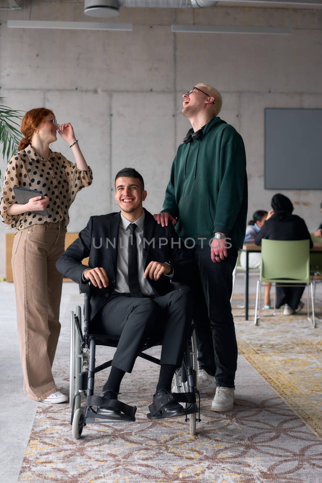 Group cheerful business colleagues, including a businessman in a wheelchair, posing together in a modern office, showcasing teamwork and inclusivity.