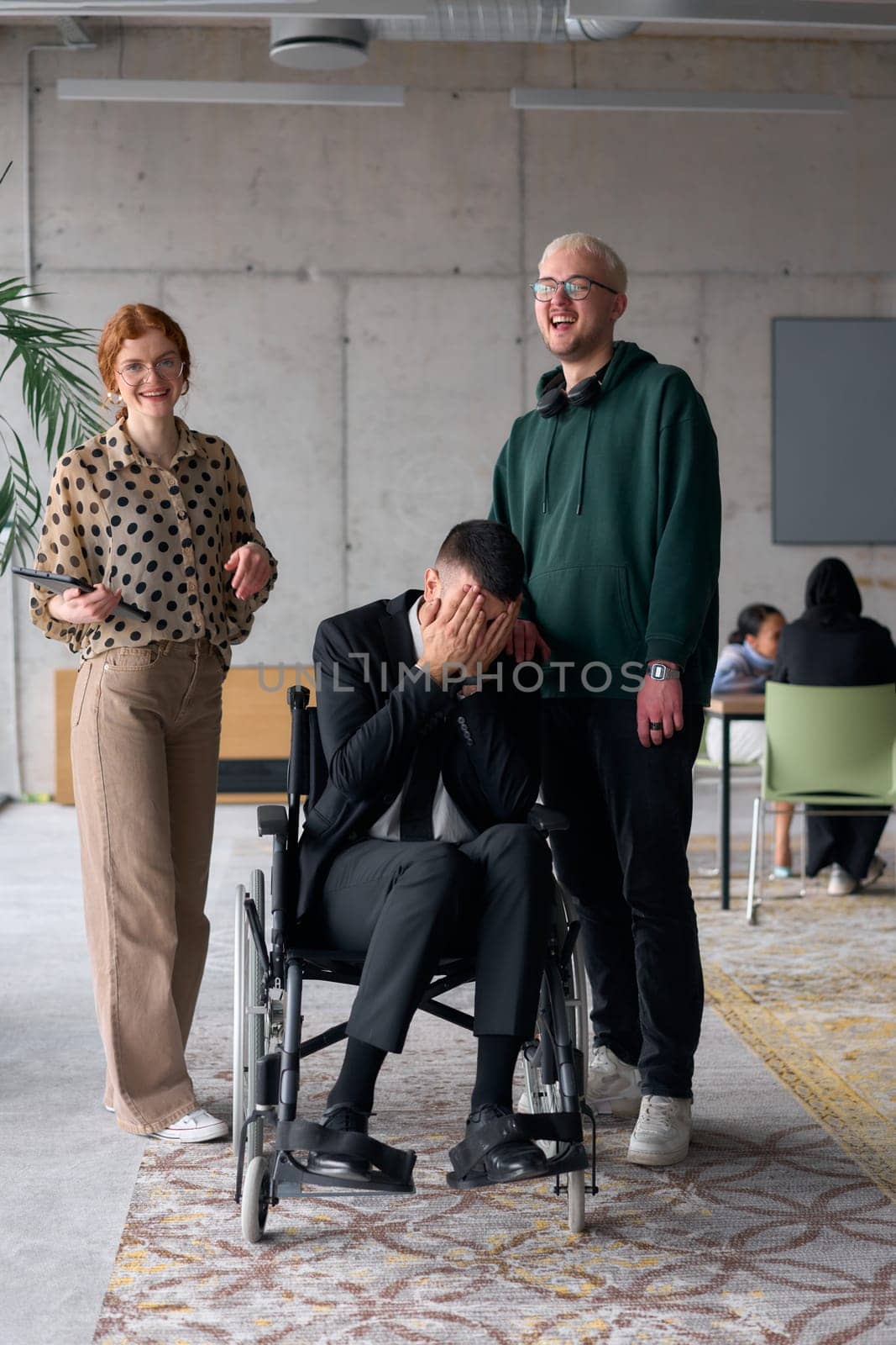 Group cheerful business colleagues, including a businessman in a wheelchair, posing together in a modern office, showcasing teamwork and inclusivity.