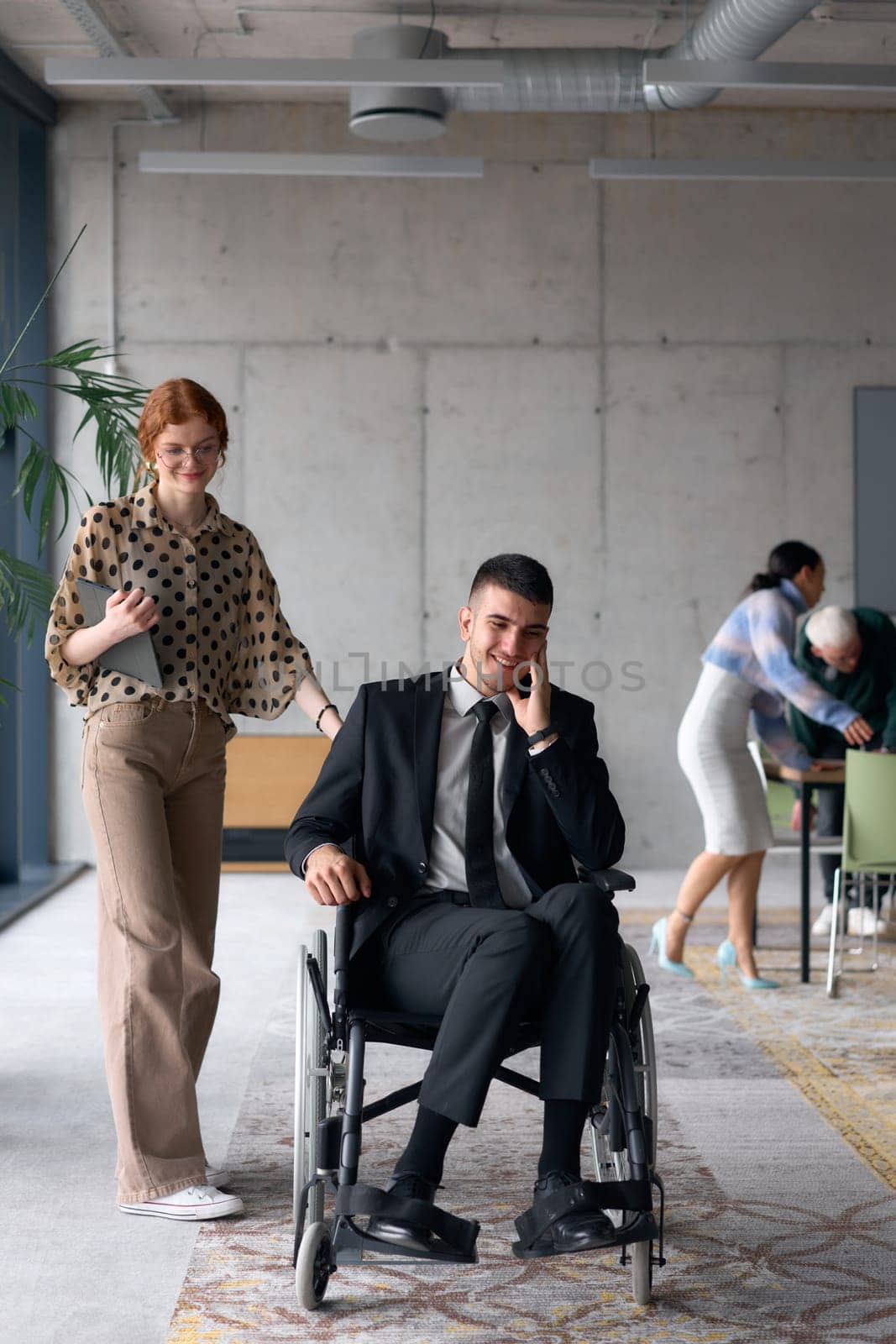 A business director in a wheelchair moves confidently through a modern office alongside his colleague, showcasing teamwork, leadership, and inclusivity in the workplace