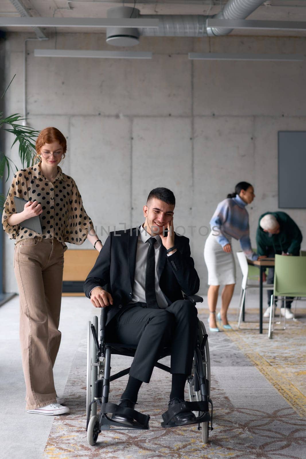 Group cheerful business colleagues, including a businessman in a wheelchair, posing together in a modern office, showcasing teamwork and inclusivity.