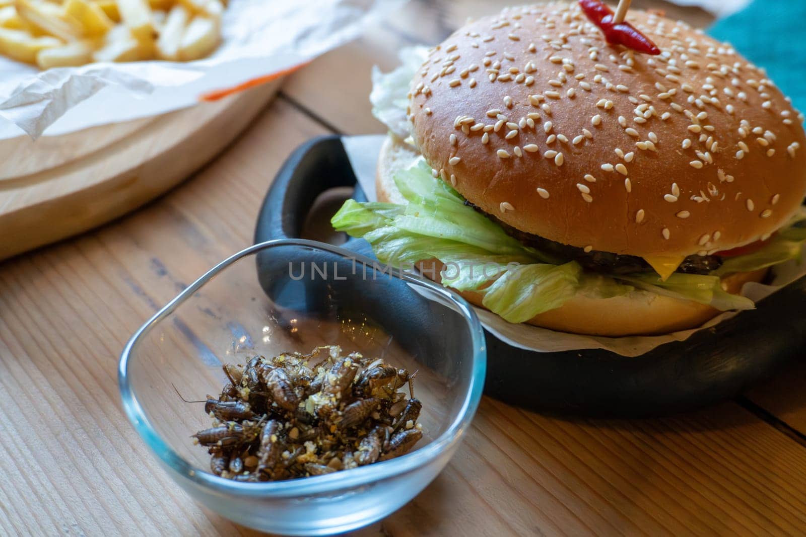 Innovative burger with insect garnish and fries on wooden table.