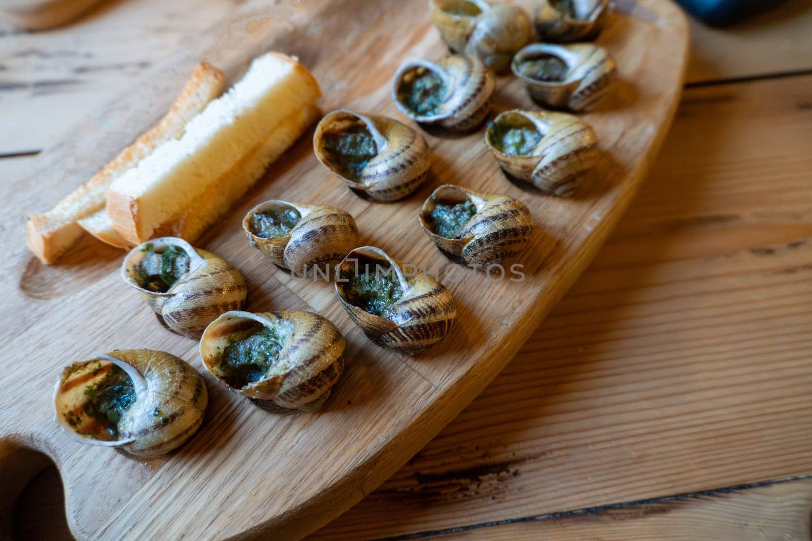 Escargot and bread on wooden tray: french culinary delicacy.