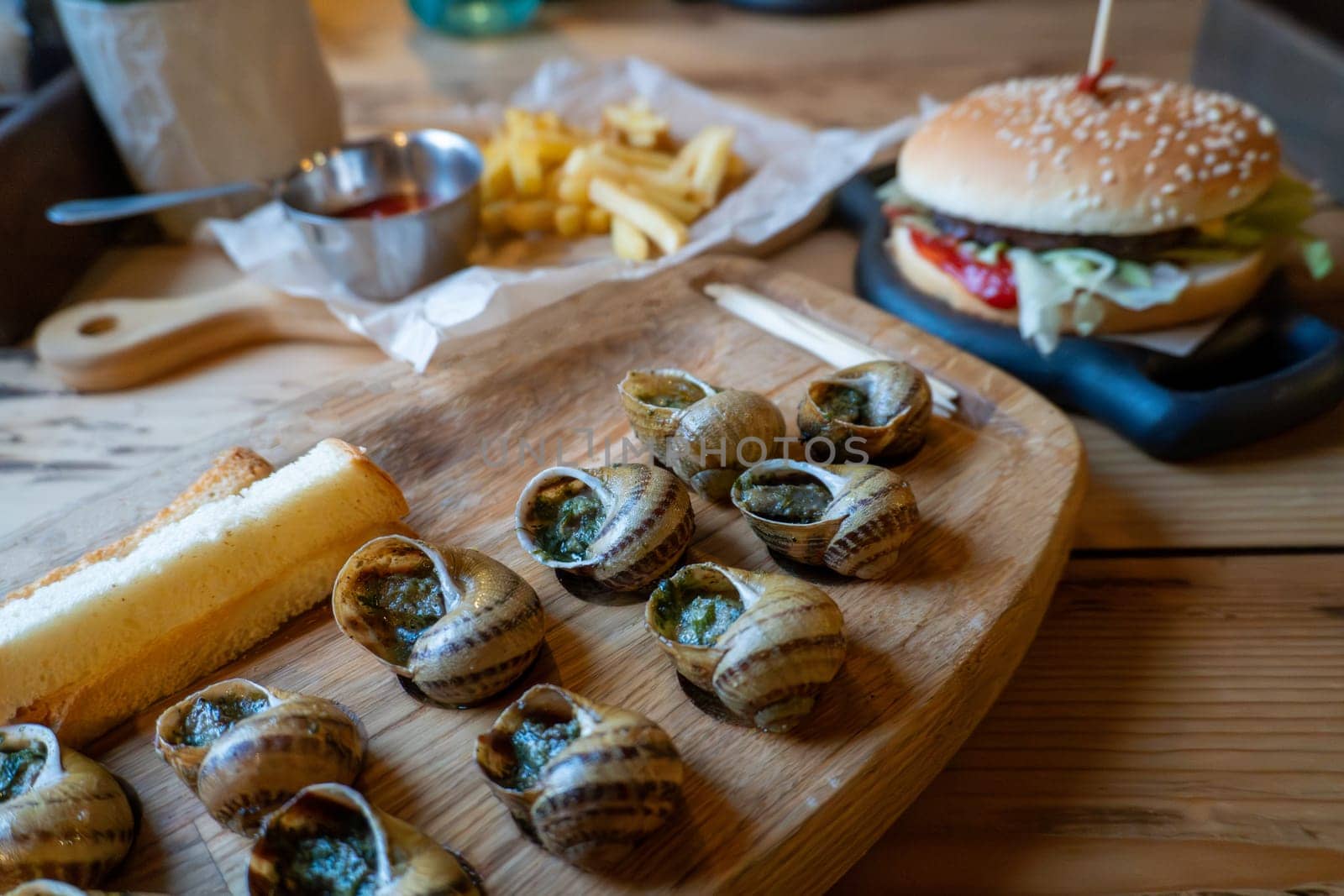 Delicious escargot and cheeseburger with fries on wooden table.