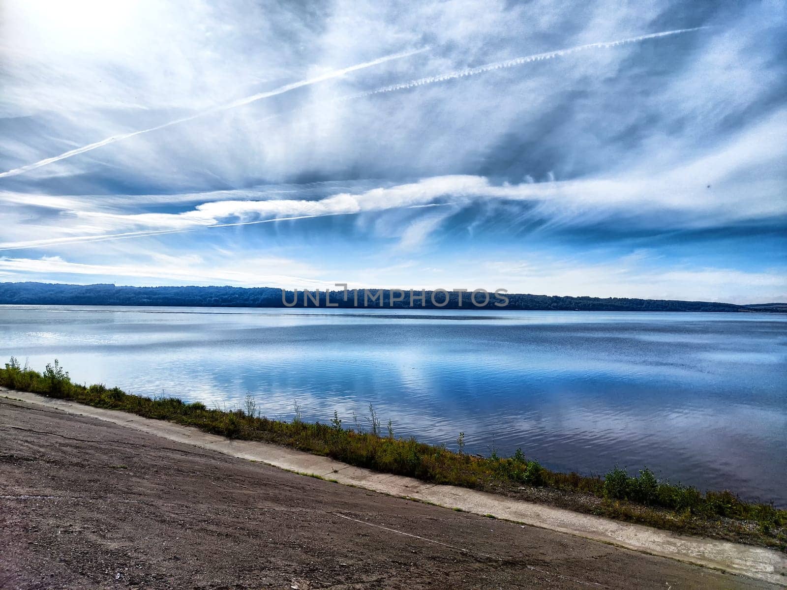 A tranquil lake reflects the dawn sky, while gentle clouds drift above and mountains frame the peaceful landscape.