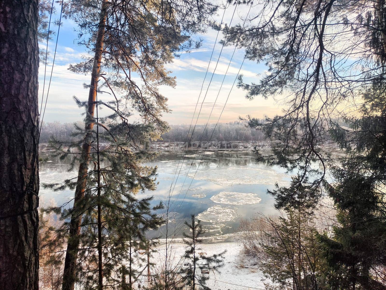 Snow and ice fragments break away in the river at early morning as spring begins, surrounded by tall trees and soft light.