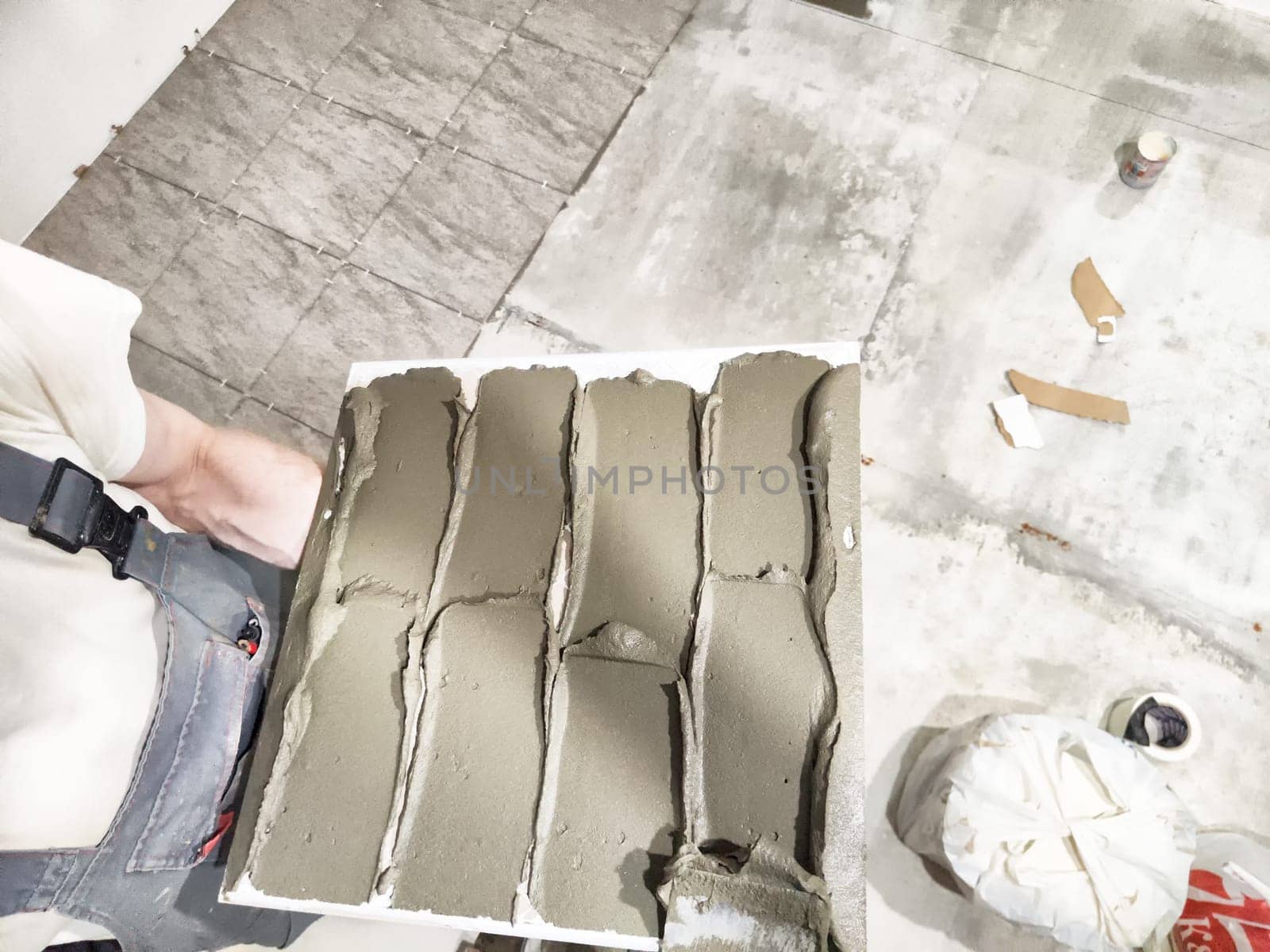 Craftsman applies tile adhesive in an indoor setting, preparing for new tile installation on the floor. Tools and materials are visible.