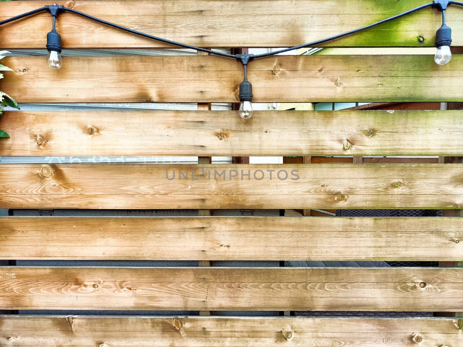 A wooden fence features horizontal planks and decorative string lights, offering a cozy backdrop ideal for events or celebrations.
