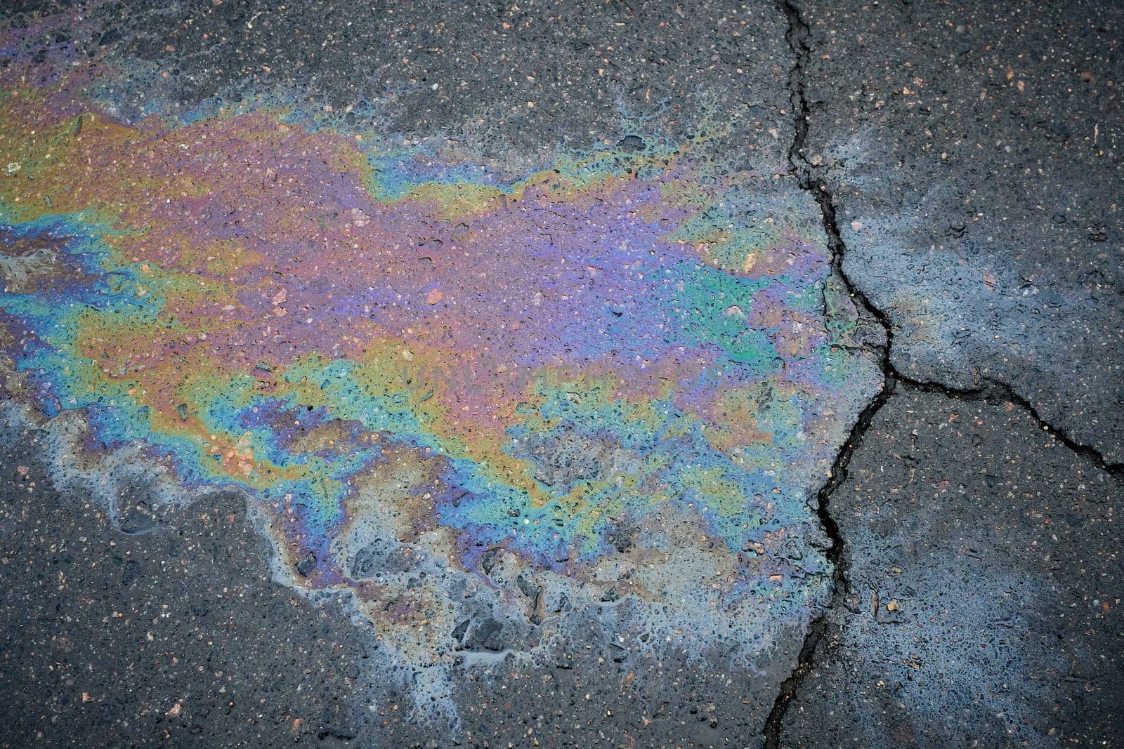 Gasoline or oil spill creating rainbow colors on cracked asphalt road.