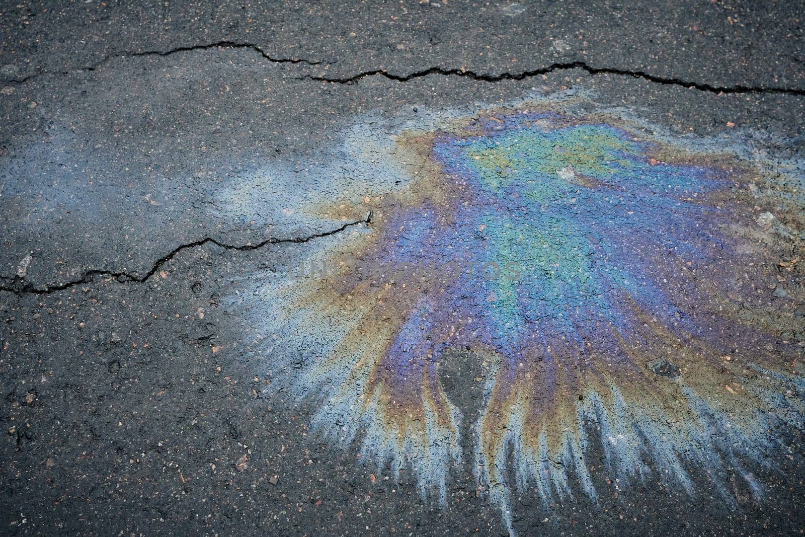 Colorful gasoline or oil spill creating a rainbow effect on cracked asphalt road, highlighting environmental pollution and road damage