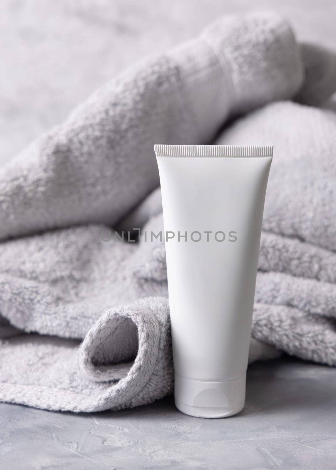 White blank cosmetic squeeze cream tube near light grey towel in bathroom top view, brand packaging mockup. Natural herbal cosmetic product for daily facecare, copy space