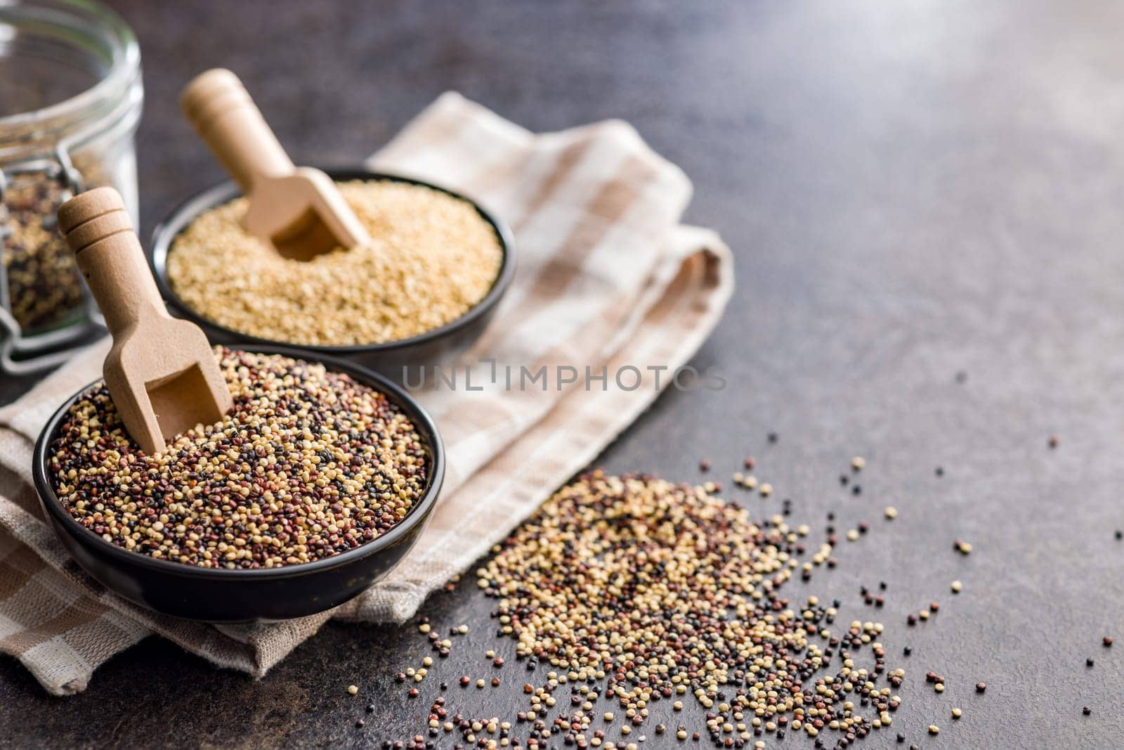 Mixed uncooked quinoa seeds in bowl on a black table.