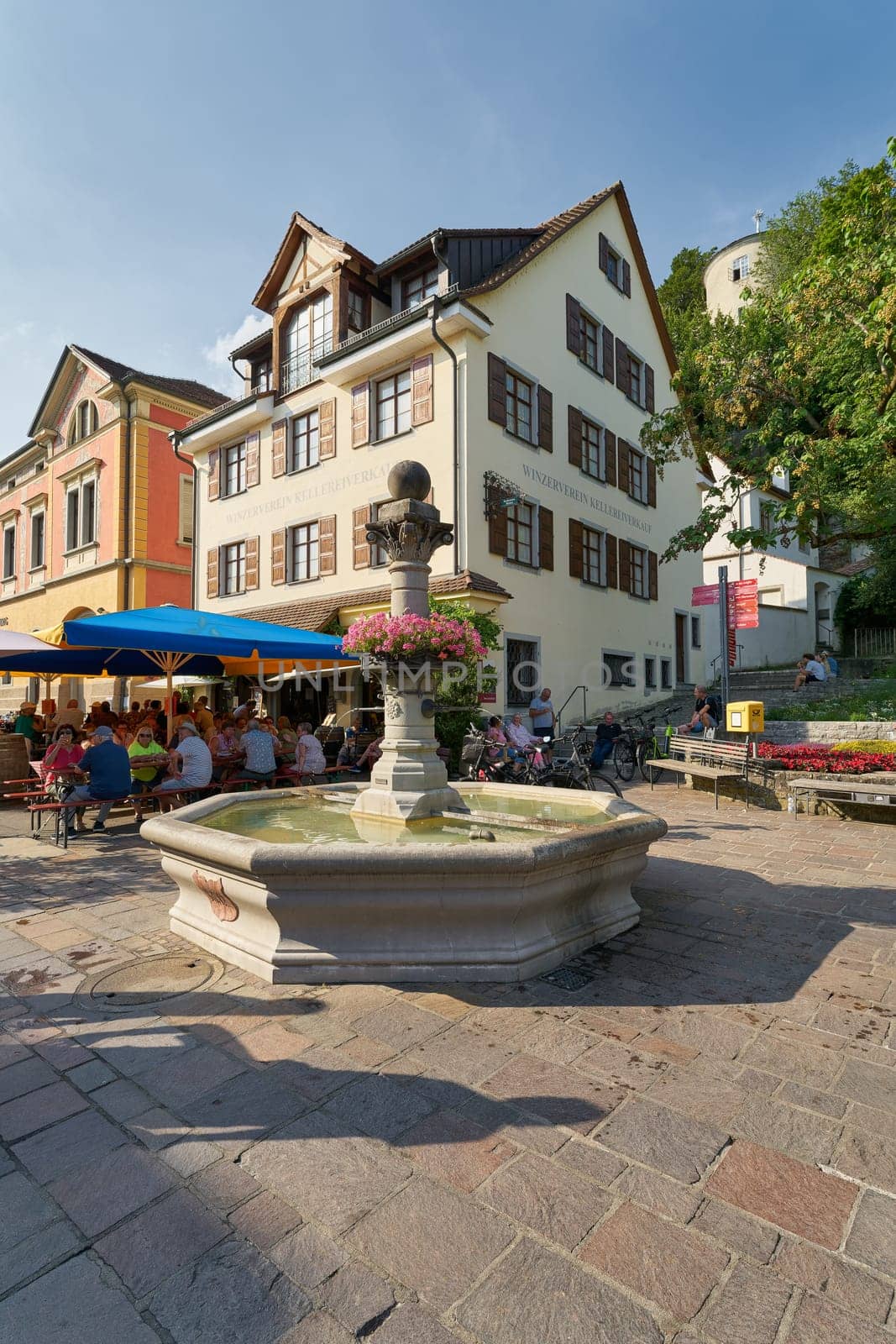 Meersburg, Germany – August 03, 2024: Historical fountain, Brunnen des Altertum and tourists at a wine tavern in Meersburg on Lake Constance, Bodensee in Germany