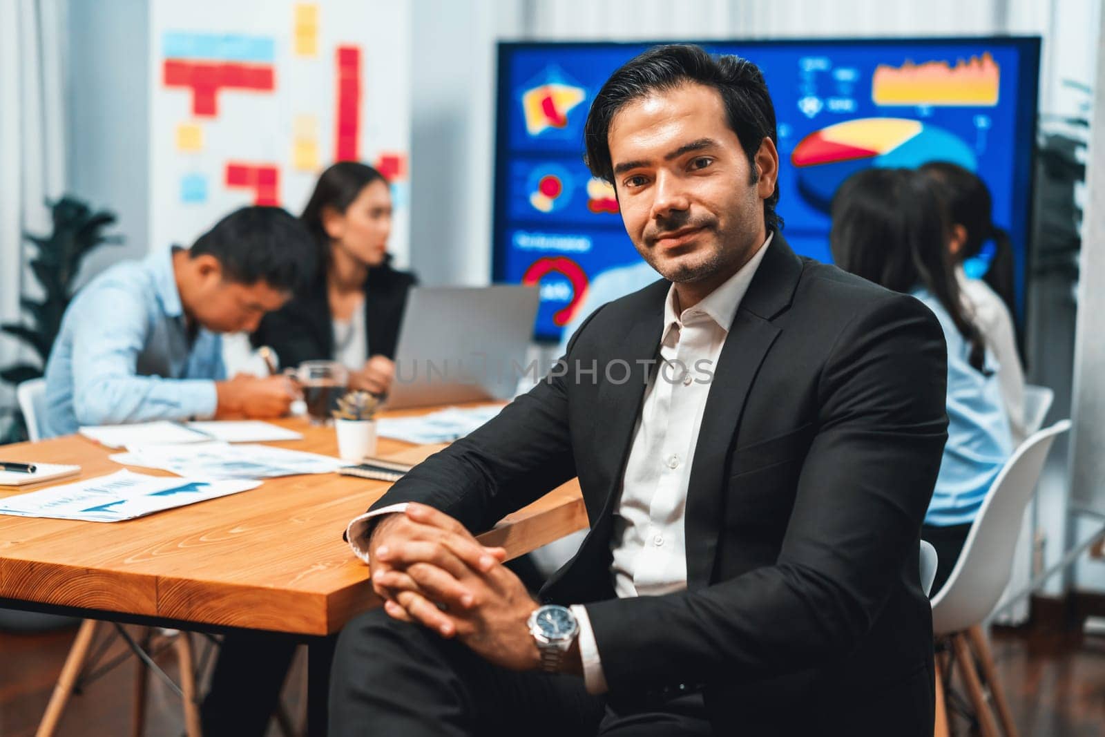 Portrait of businessman or analyst looking at camera with his colleague analyzing data analysis in dynamic business strategy investment planning meeting. Meticulous