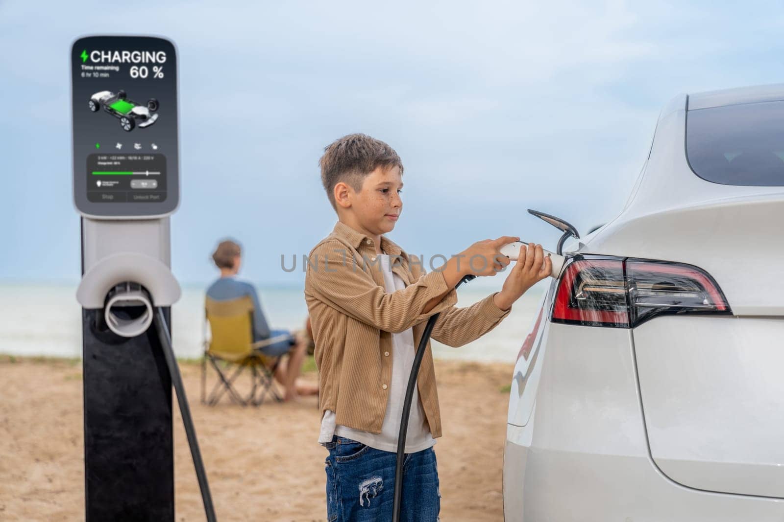 Family vacation trip traveling by the beach with electric car, little boy recharge EV car while his family enjoy seascape beach. Family trip with alternative energy and eco-friendly car. Perpetual