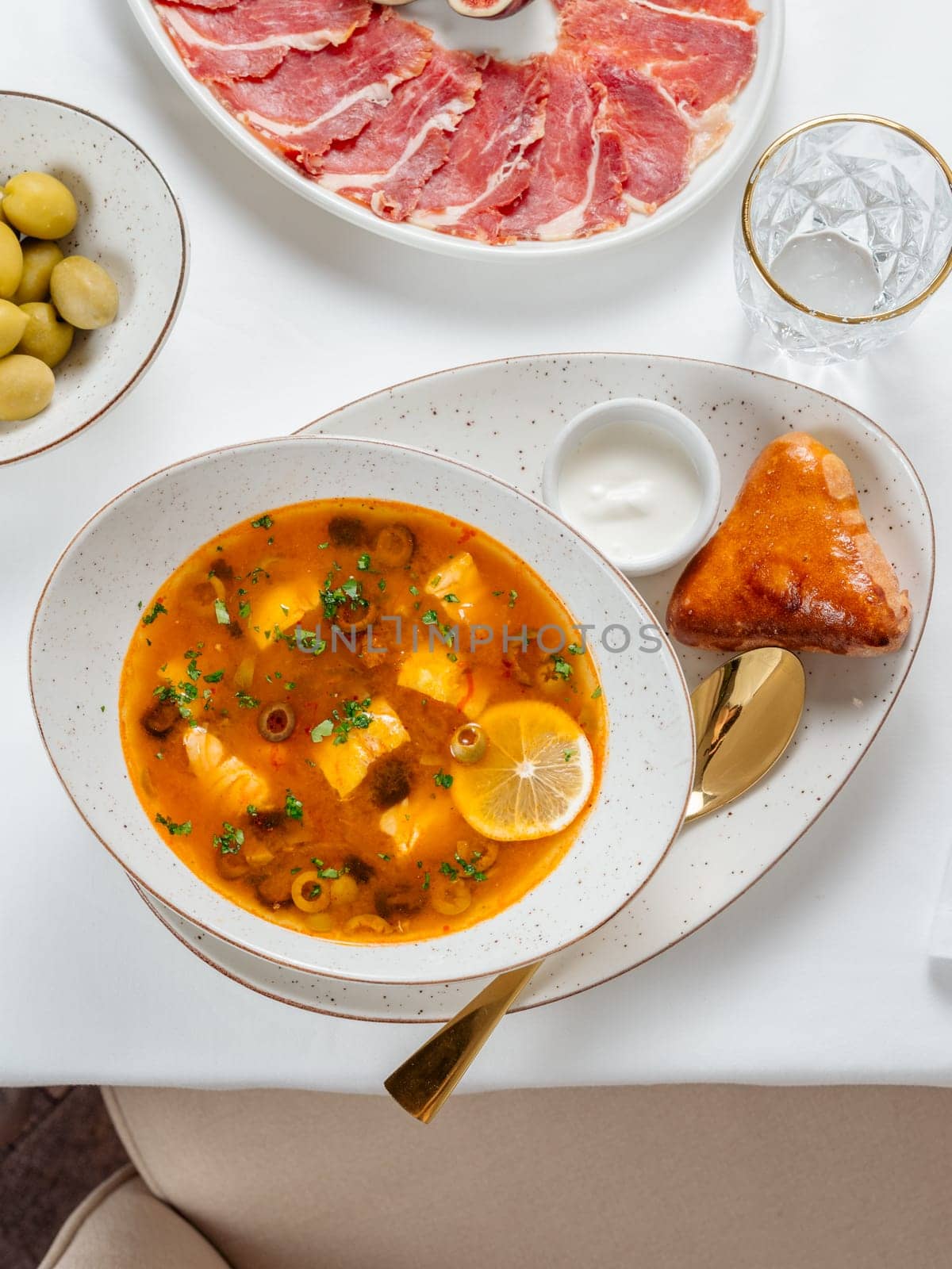 Solyanka soup with meat and olives garnished with a slice of lemon. Traditional Russian meat soup Solyanka in bowl on restaurant table. Top view or flat lay.