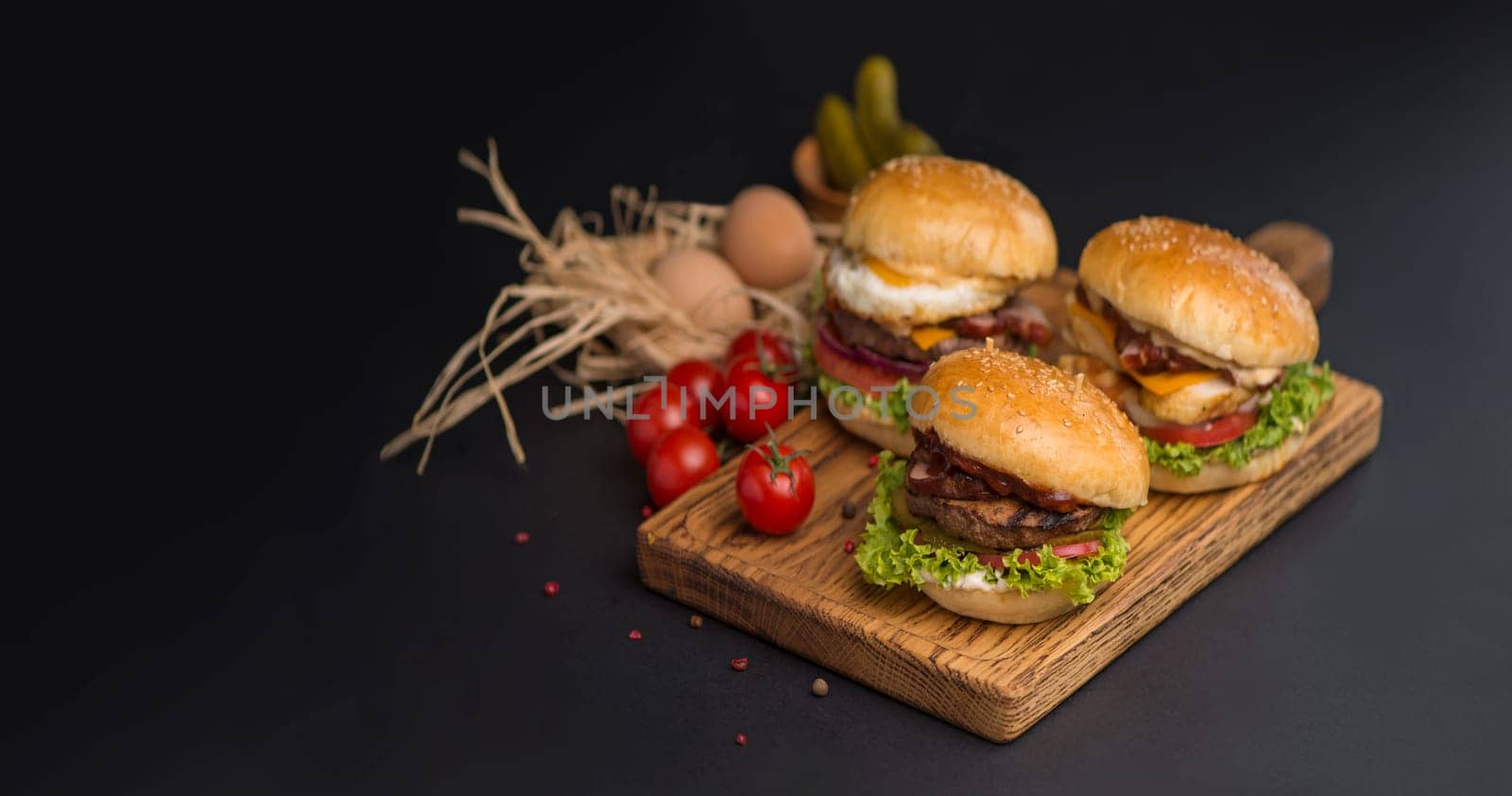 Close-up of a delicious fresh homemade burgers with lettuce, cheese, onion and tomato on a rustic wooden board on a dark background by aprilphoto