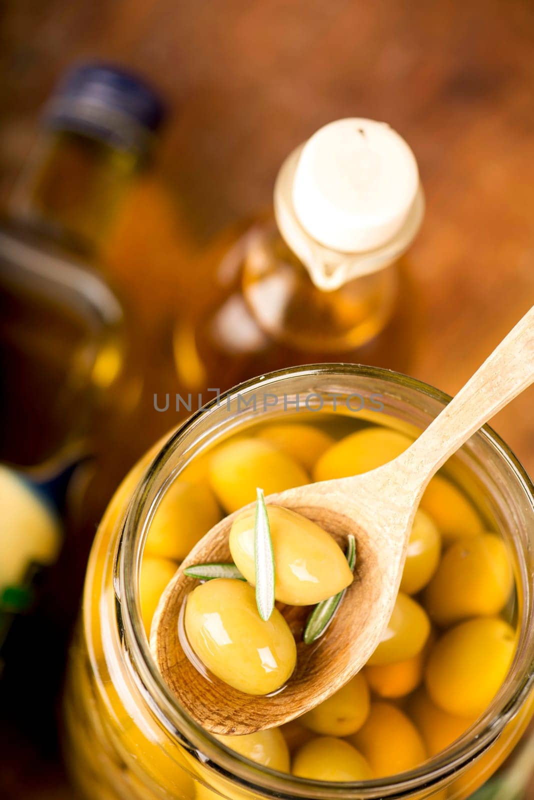 Close up green olives in bank, rosemary on a wooden background