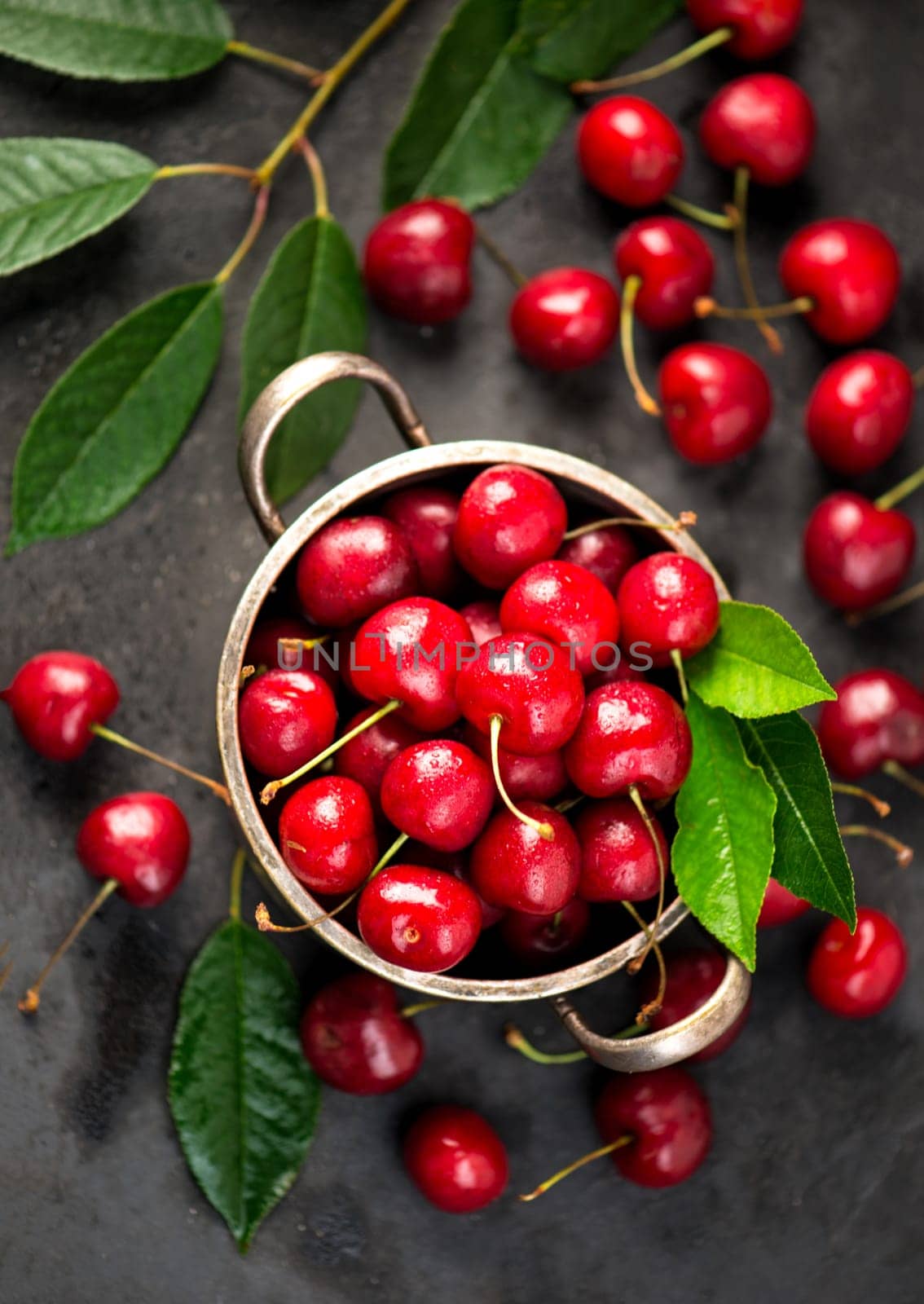 Cherry summer background. A large number of cherries with leaves on the table in a saucepan on a black background. close-up. by aprilphoto