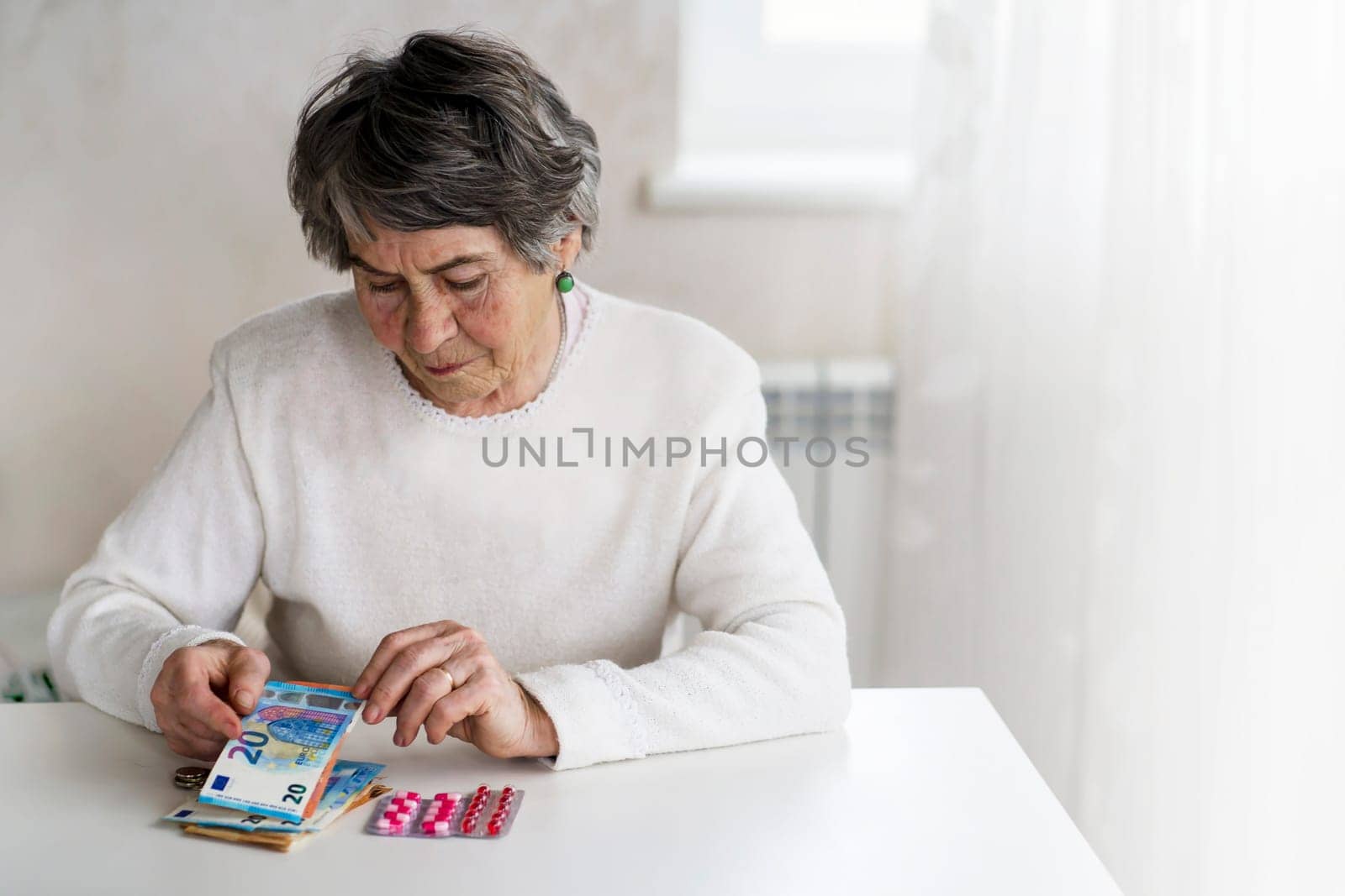 An elderly 80 year woman, a well-groomed pensioner considers her money and expenses, and saves some of it for medications and treatment. An old lady in a white sweater is planning her budget.