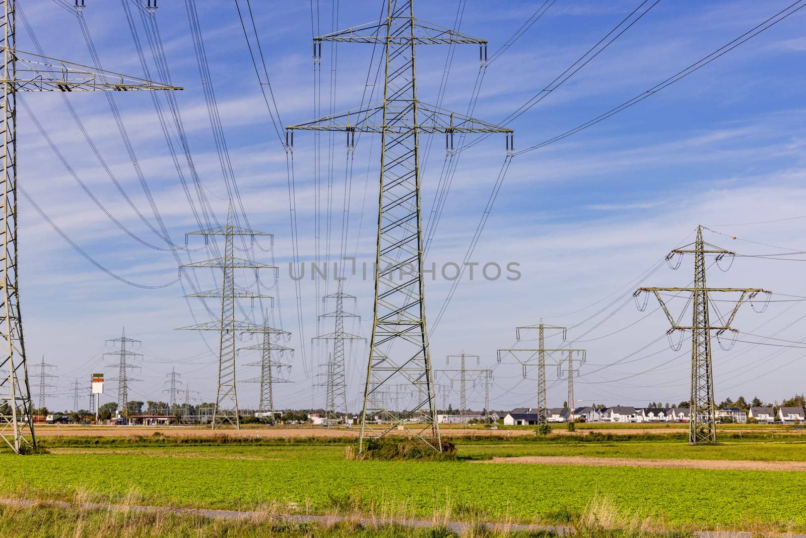 Countless power poles and power lines in nature in front of houses of a city in background