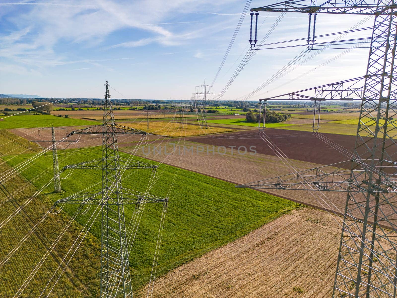 Aerial shot of between several power pylons with many overhead power lines and power lines to the horizon in energy transition in Germany