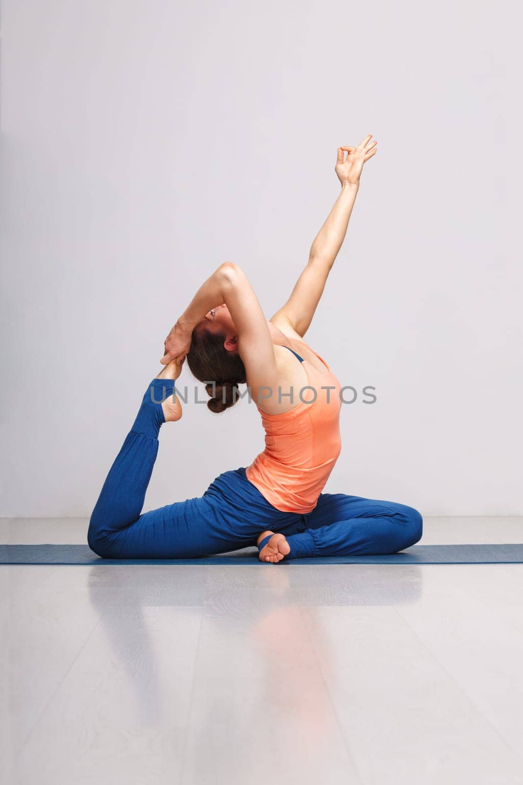 Woman doing Hatha yoga asana Eka pada rajakapotasana - one-legged king pigeon pose on yoga mat on yoga mat in studio on grey bagckground