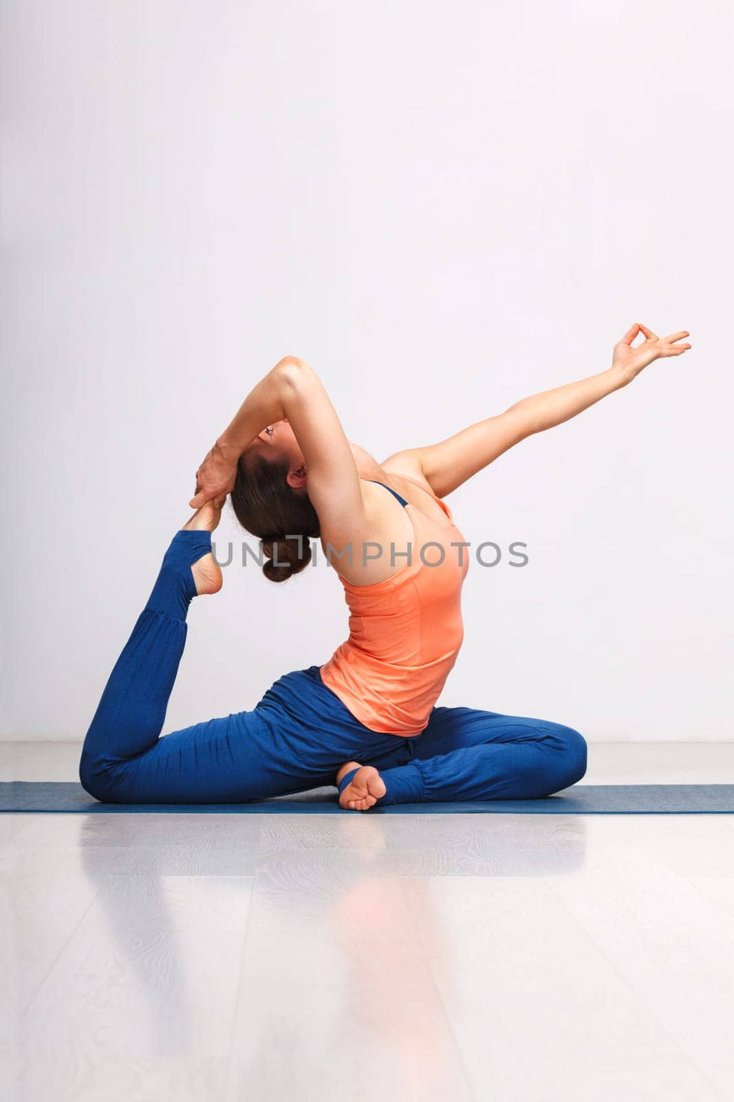 Woman doing Hatha yoga asana Eka pada rajakapotasana - one-legged king pigeon pose on yoga mat on yoga mat in studio on grey bagckground