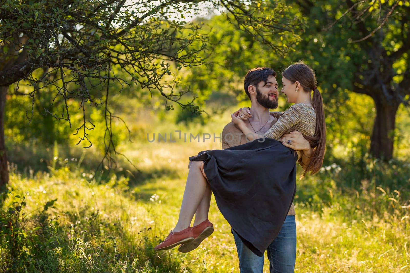 guy carries his girlfriend in his arms in a summer park