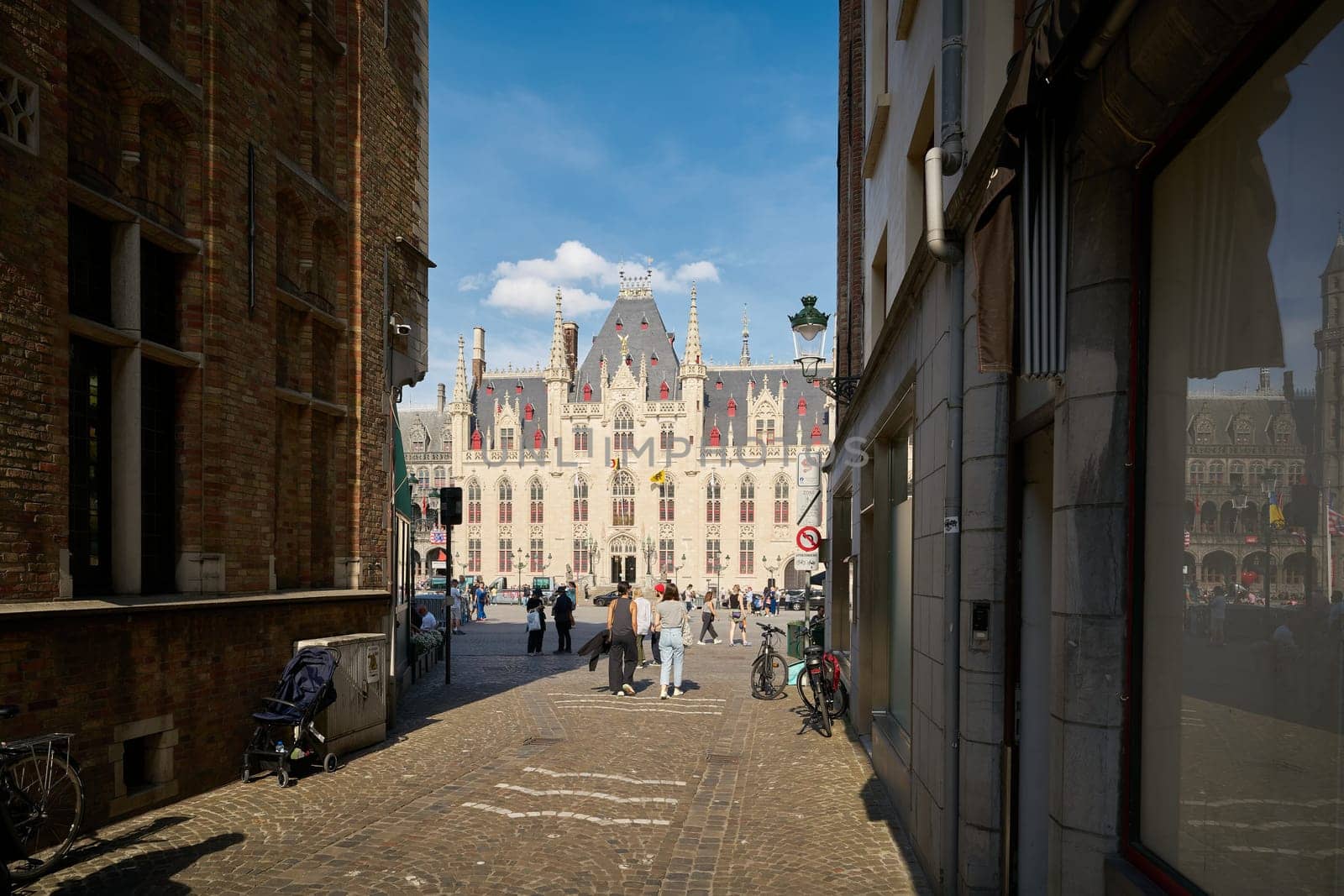 Bruges, Belgium – May 12, 2024: View through an alley to the market square, Grote Markt with the Provincial Palace in Bruges, Belgium