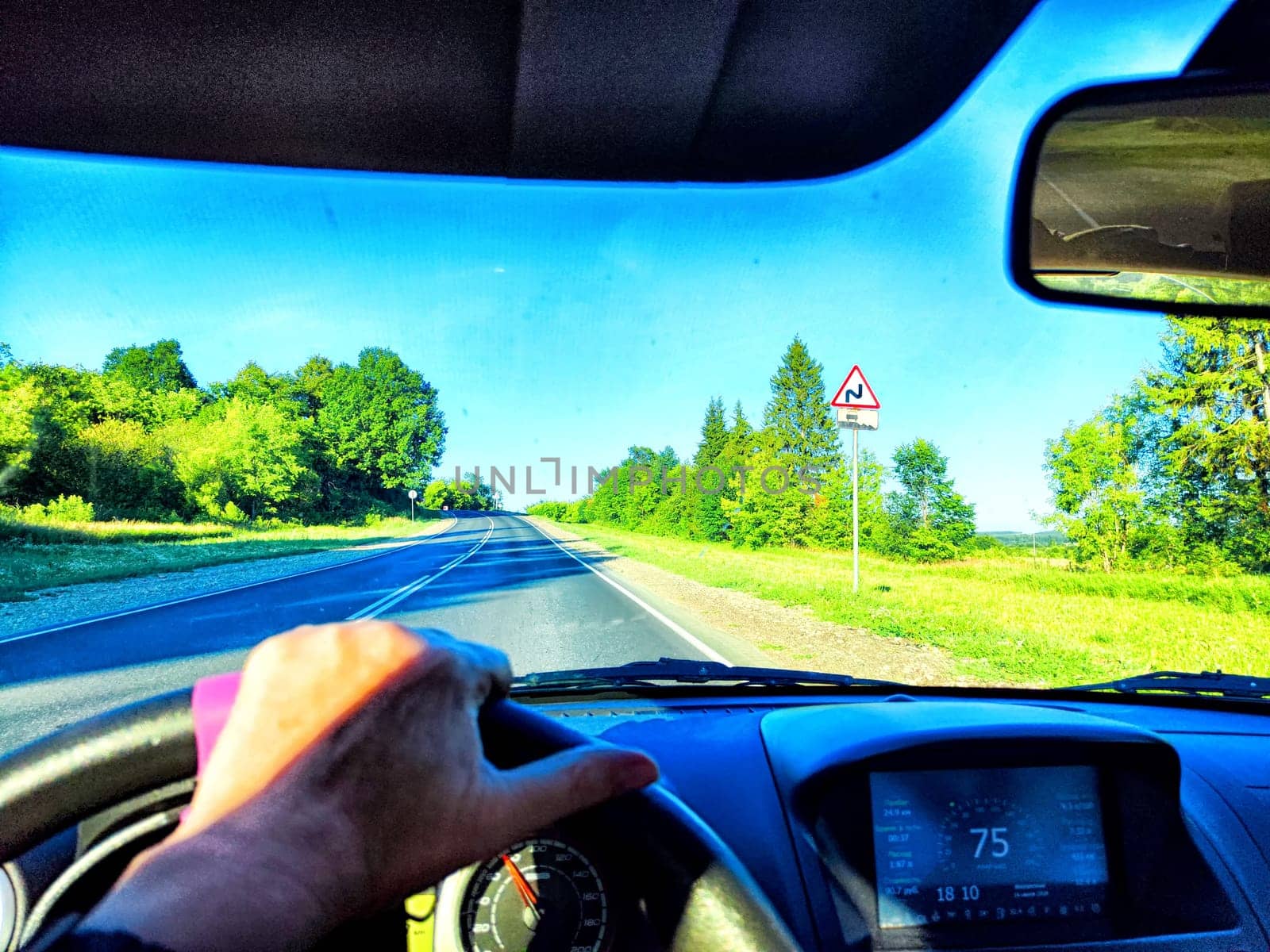 A driver navigates a scenic road surrounded by lush greenery and blue sky.