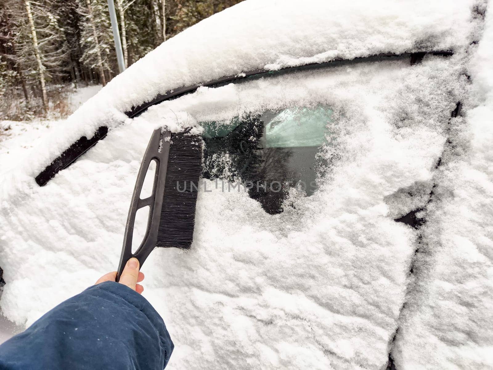 A person sweeps off thick snow from a car with a brush while enduring the chilly winter temperatures, preparing for a drive.