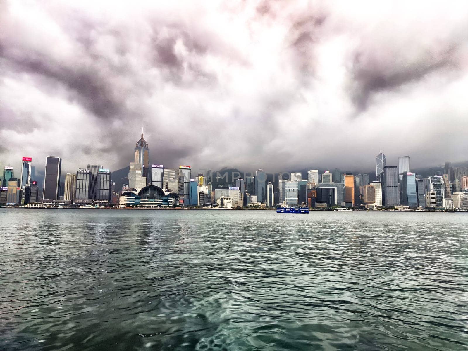 Hong Kong - April 06, 2024: Victoria Bay showcases the skyline of Hong Kong shrouded in fog, with towering buildings obscured by clouds. The water reflects the muted skyline on this overcast day.