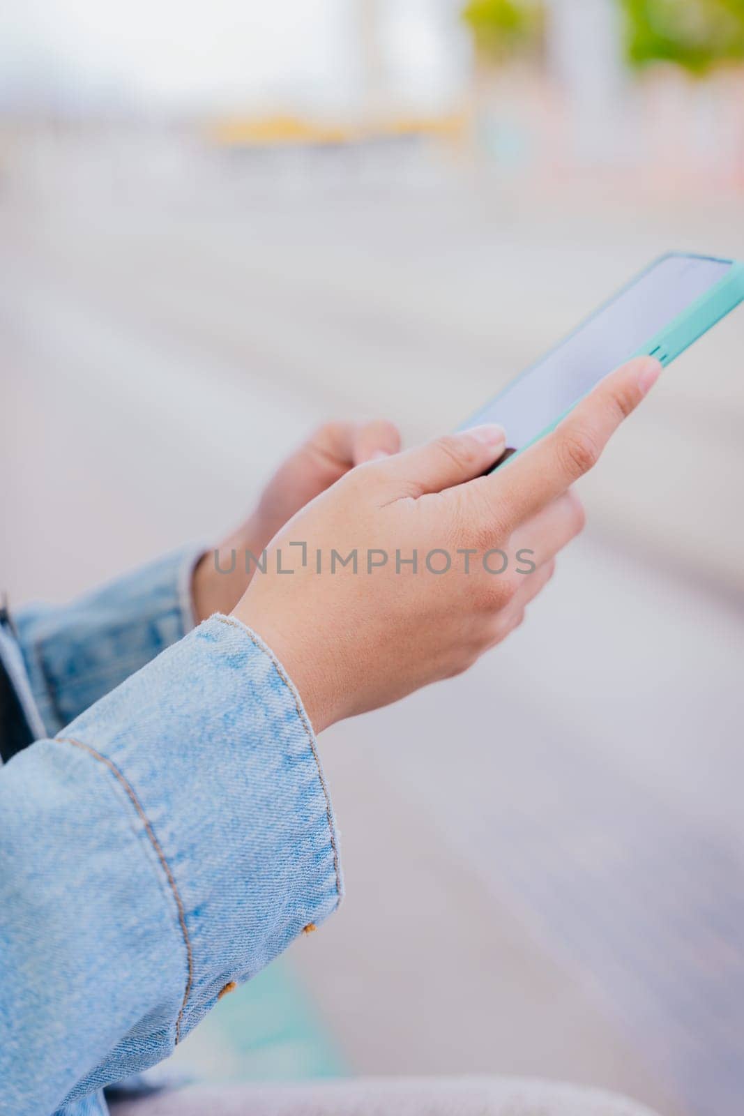 Close-up of a person wearing a denim jacket holding and using a smartphone in an urban environment. The image represents digital communication, technology, and modern connectivity.